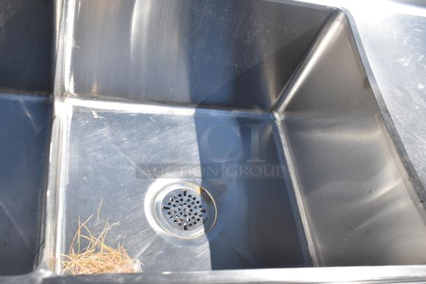Stainless steel commercial 3 bay sink with dual drain boards, featuring visible surface wear and a central drain.