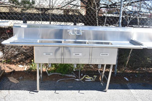 Commercial 3 bay sink with dual drain boards, featuring labeled "Wash," "Rinse," and "Sanitize" sections in stainless steel.