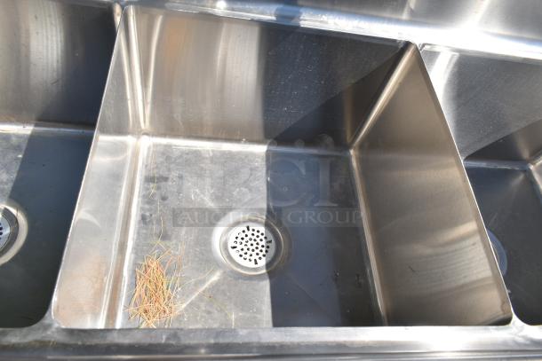 Commercial 3 bay stainless steel sink with dual drain boards, showing three basins and two drain covers, in used condition.