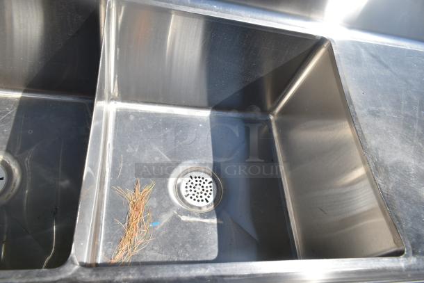 Commercial 3 bay stainless steel sink with dual drain boards, showcasing moderate wear. Contains visible rust and debris.