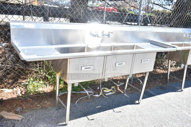 Commercial 3 bay sink with dual drain boards, stainless steel, labeled “Wash,” “Rinse,” “Sanitize,” in used condition.