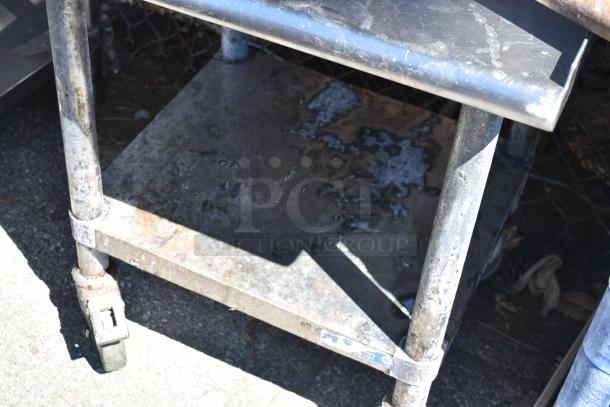 Commercial equipment stand with under shelf, on heavy-duty casters. Used condition with visible wear and surface marks.