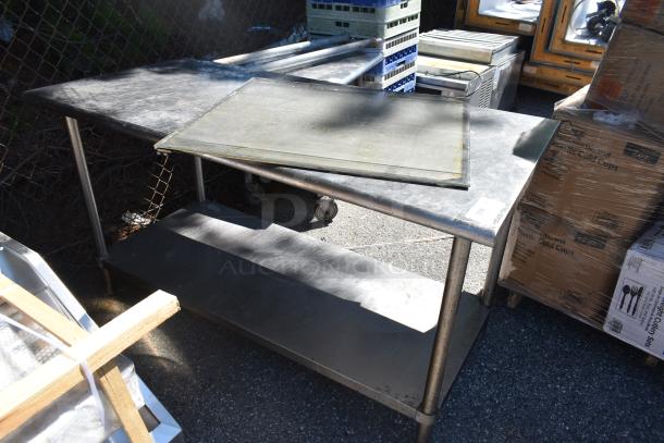 Commercial metal table with lower shelf, weathered surface, caster wheels, ideal for kitchen use, shows signs of use.
