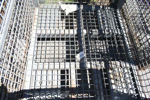 Wire cage with metal grid design, visible rust, and industrial use wear. Features attached labels with barcodes.