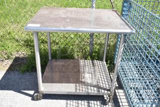 Commercial stainless steel table with under shelf, on heavy-duty casters. Good condition, ideal for industrial use.