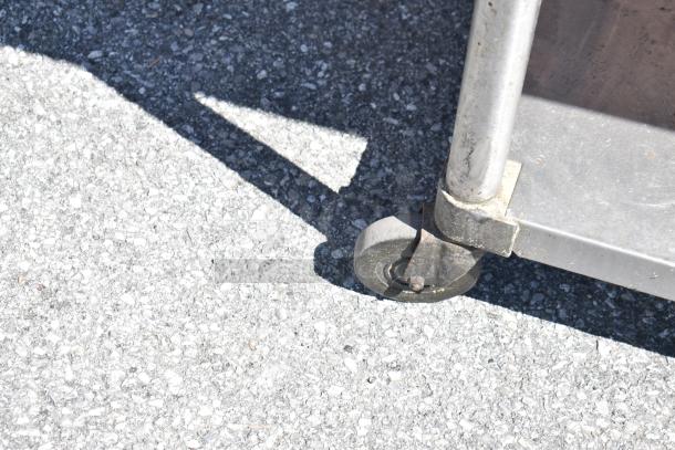 Commercial table with under shelf on durable casters, shown on concrete. Ideal for versatile, mobile use.