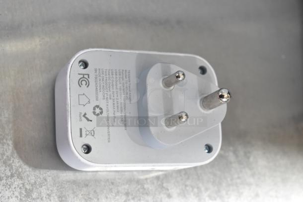 A white electrical adapter with two round prongs and several printed certifications and specifications on its surface.