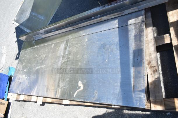 Three metal panels stacked on a wooden pallet, showing signs of wear and exposure. Suitable for industrial use.