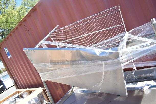 Three stainless steel furniture items including two tables and one work counter with doors, wrapped in plastic, by a storage container.