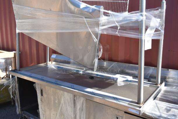 Three metal items including two tables and a work counter with doors, wrapped in plastic. Auction item, bid for triple value.