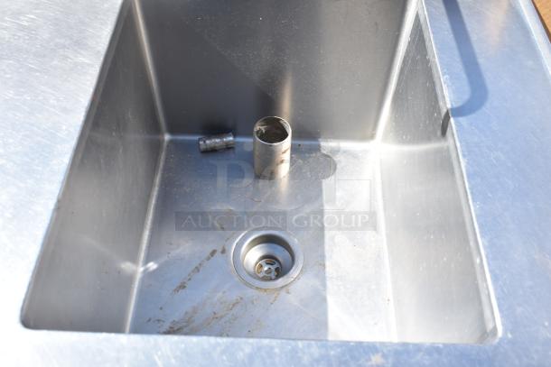 Commercial counter with stainless steel sink bay, slightly worn, includes plumbing fittings and drain, ideal for kitchen use.