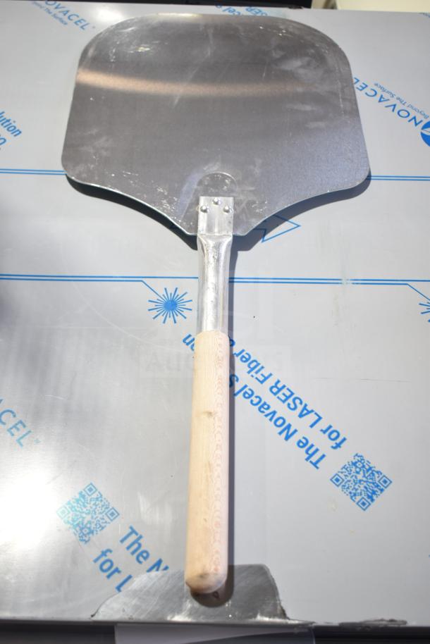 Metal pizza peel with wooden handle, part of a 28-item auction set including peels and plate chargers. Handle shows slight wear.