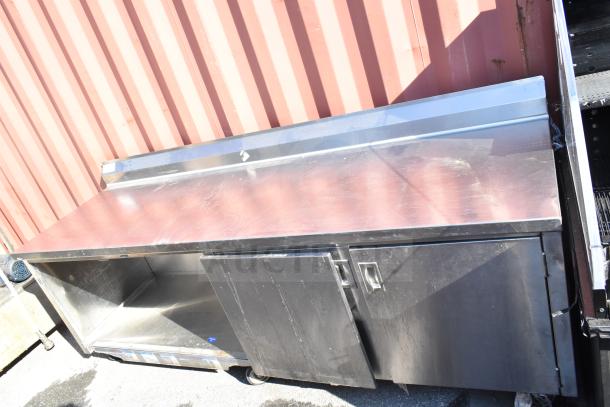 Stainless steel commercial counter with doors and under shelf, featuring ample storage. Visible wear, sturdy construction.