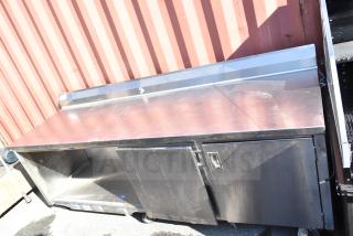 Stainless steel commercial counter with doors and under shelf, featuring ample storage. Visible wear, sturdy construction.