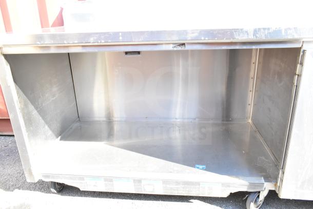 Commercial stainless steel counter with doors and under shelf, on casters, used condition, ideal for kitchen storage.