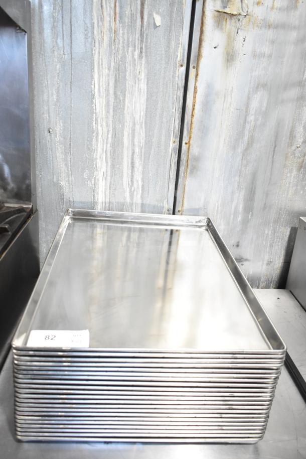 Stack of 21 full-size baking pans in stainless steel. New condition, with a label marked "82" indicating auction lot. 