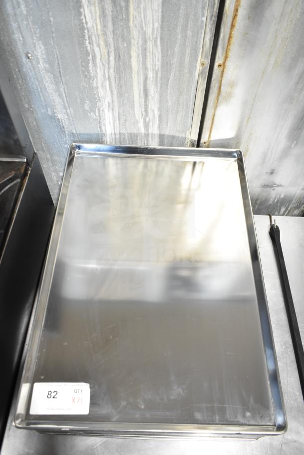 21 full-size stainless steel baking pans, new condition, quantity tag indicates "21 times your bid," shiny and reflective surface.