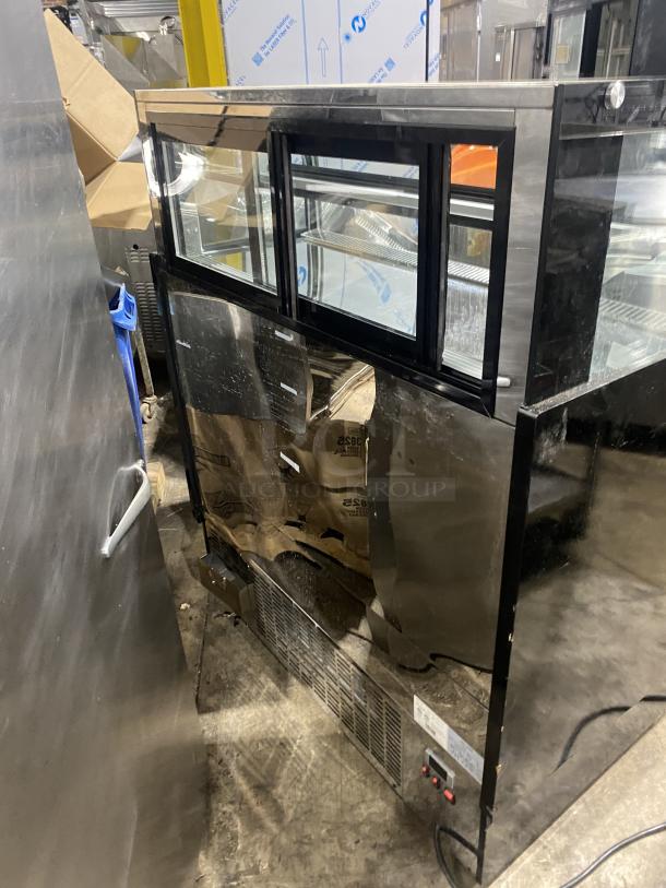 Commercial black dual service glass display case, refrigerated, with visible stainless steel elements, shows minor wear.