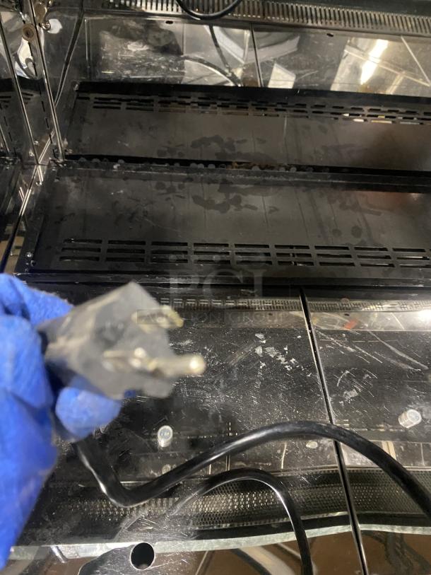 Commercial black dual service display case merchandiser, glass refrigerated, shows plug detail, moderate wear visible.