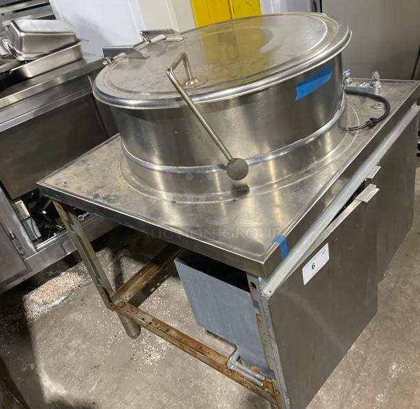 Stainless steel steam kettle with power tilt on sturdy legs. Commercial grade, used condition, with visible wear.