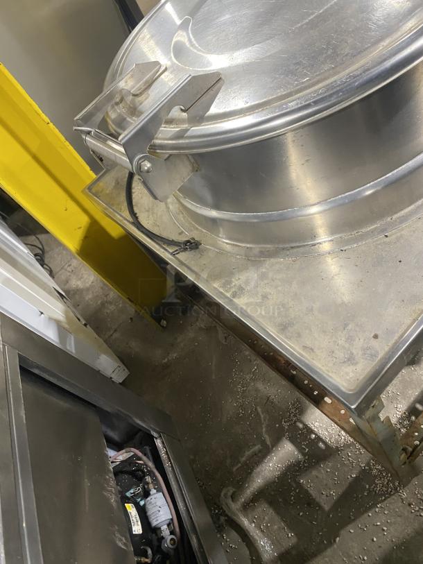 All stainless steel steam kettle with power tilt, mounted on legs. Features secure lid and rugged build, ideal for commercial use.