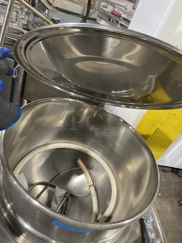 Commercial stainless steel steam kettle with power tilt, on legs. Features open lid, interior heating elements. Excellent condition.