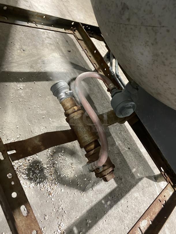 Commercial stainless steel steam kettle with power tilt feature, visible pipes and connectors, mounted on legs, slightly worn condition.