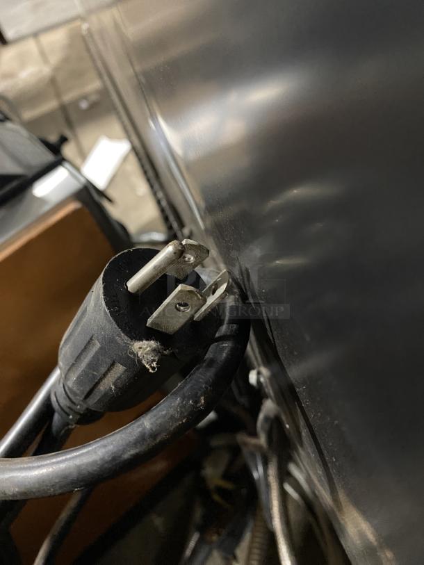 Power cord of True GDM-49F-HC-TSL01 commercial freezer, showing plug detail; part of stainless steel and black body visible.