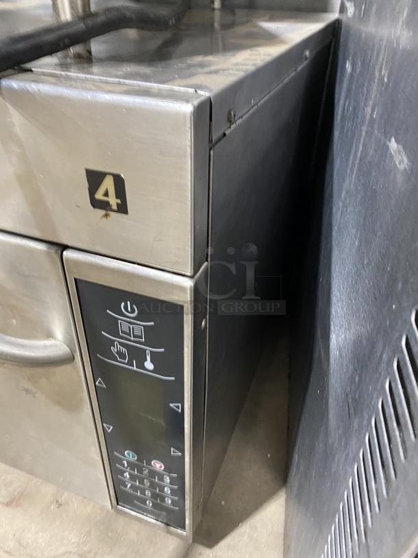 A stainless steel Amana commercial microwave oven, 208-230V, keypad and number 4 label visible, shows signs of wear.