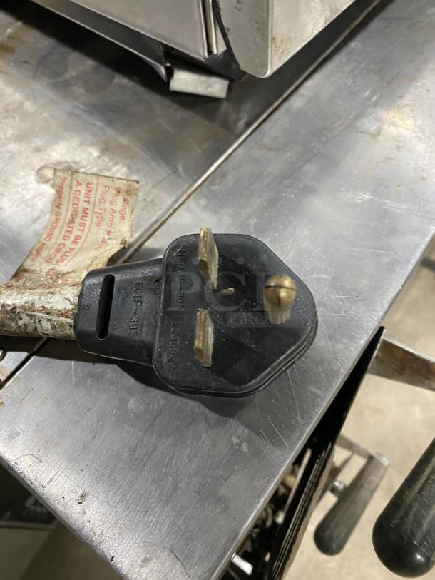 Amana Commercial Stainless Steel Microwave Oven 208-230V, visible power cord and plug, on metal surface.