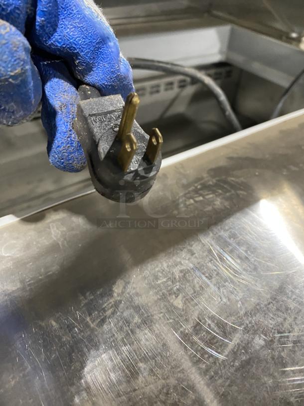 Close-up of stainless steel surface and power plug for Asber Model APTS7218 prep table refrigerator, on casters.