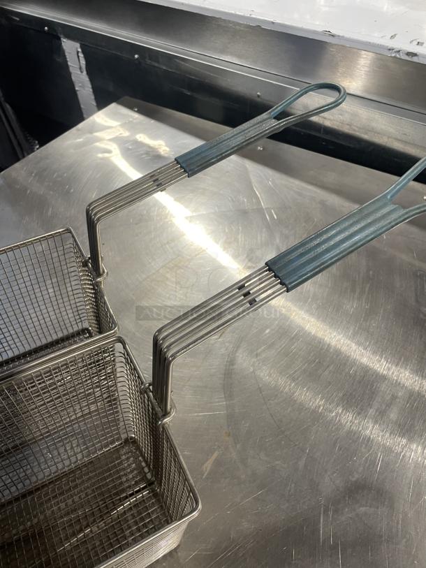 Two commercial deep fryer baskets with durable wire mesh and metal handles on a stainless steel surface.