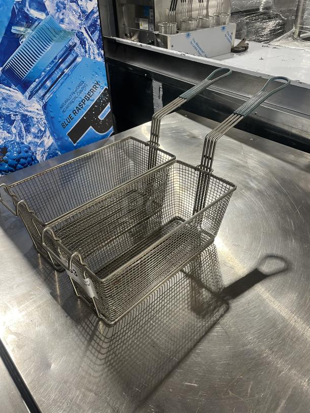 Two commercial deep fryer baskets with metal mesh design, long handles, and sturdy construction, in good condition.