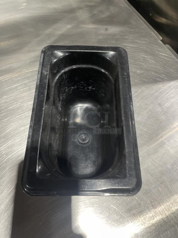 Commercial black plastic food pan on metal surface, rectangular, in good condition. Perfect for kitchen use.