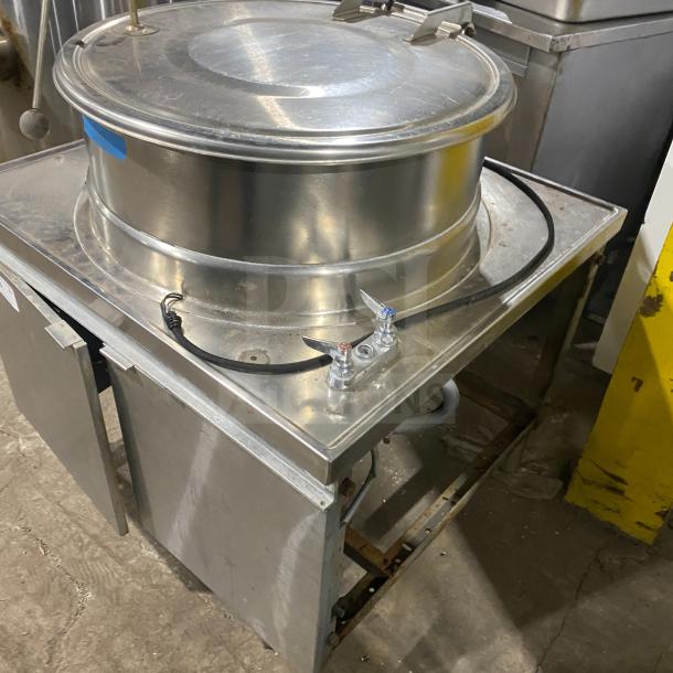 Commercial stainless steel steam kettle on legs with power tilt feature. Used condition, industrial setting.
