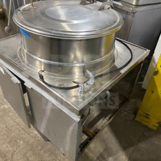 Commercial stainless steel steam kettle on legs with power tilt feature. Used condition, industrial setting.