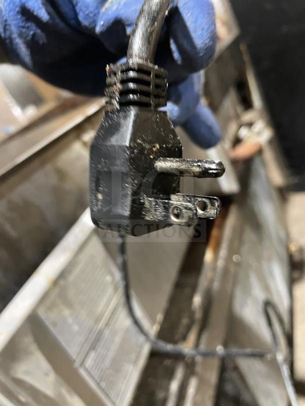 Close-up of a power plug for a Kelvinator KCHCB48R chef base. Gloved hand holding plug, showing metal prongs.