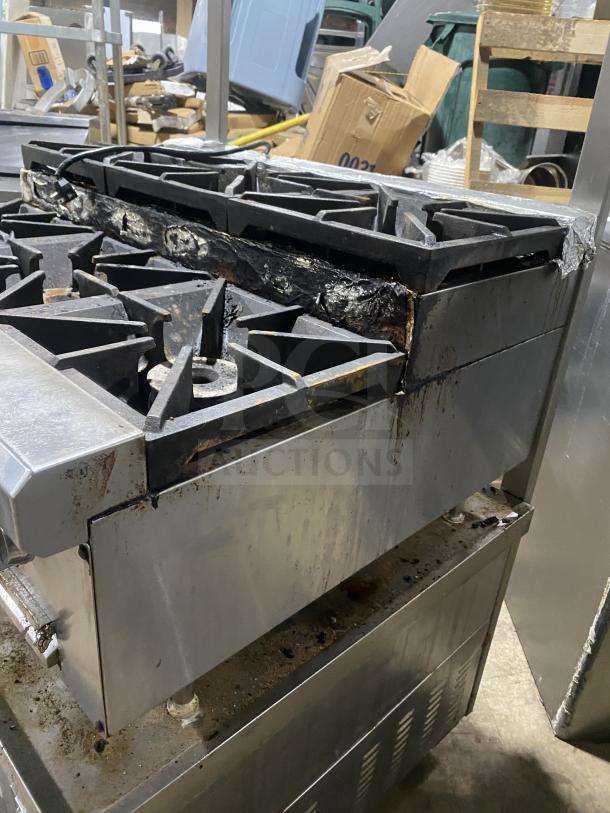 Stainless steel 6-burner gas range on legs, used condition, showing signs of wear and rust. Commercial-grade.