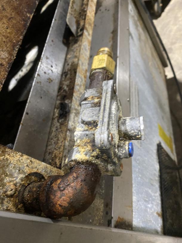 Close-up of a rusted gas connection on a stainless steel commercial 6-burner range. Visible signs of wear.