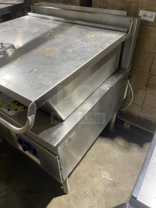Cleveland stainless steel gas tilt skillet, commercial use, on legs. Visible knobs and slight surface wear.