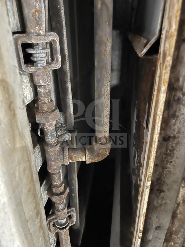 Rusted and corroded pipes connected to a commercial oven unit, showing wear and oxidation.