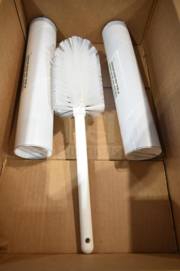 Cardboard box containing a white cleaning brush and two cylindrical white packages with visible text labels.