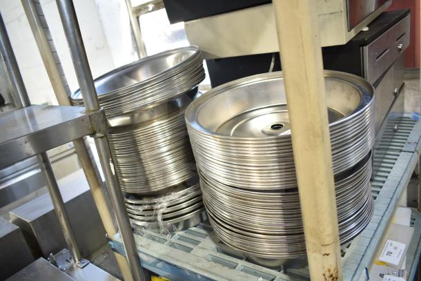 40 metal dome covers stacked on shelves, shiny and in good condition, ideal for catering or food service use.