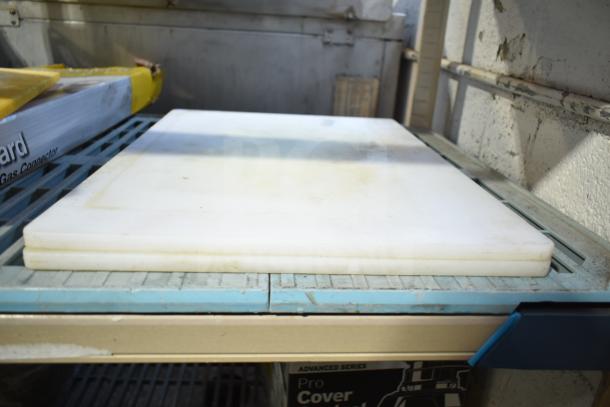 Four white plastic cutting boards stacked on a metal shelf, showing moderate wear and discoloration. Auction item.