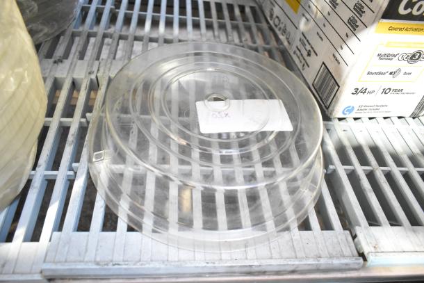 20 clear poly dome covers stacked on a metal shelf, labeled "X20". New condition, ideal for food service use.