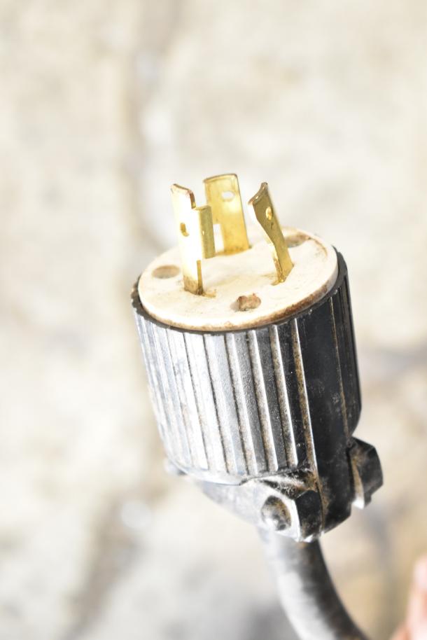 Plug for Brasilia OPUS-R-D-2 espresso machine, showing three brass prongs on a black and white connector, part of 220V system.