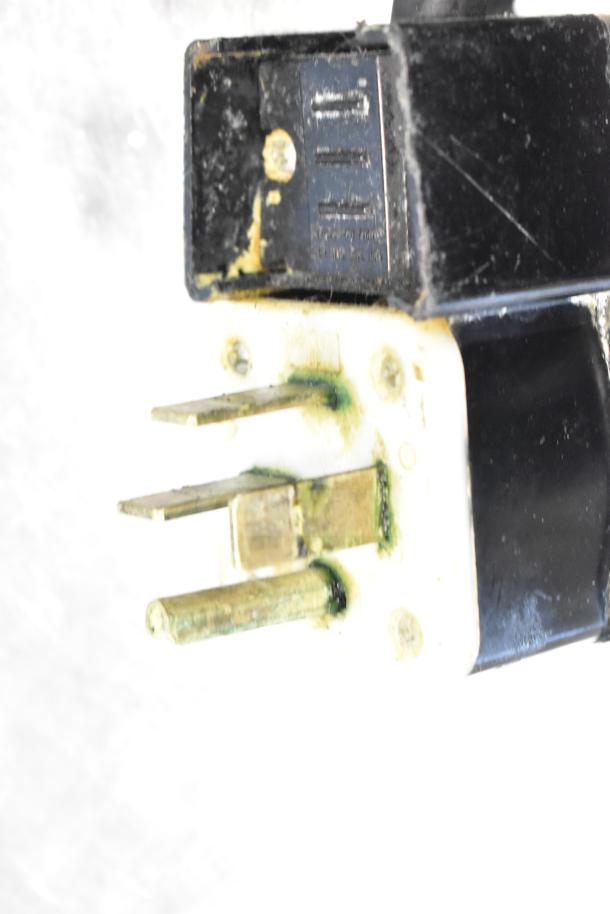 Close-up of a Fri-jado TDR7-P rotisserie oven power plug. White and black plastic with green discoloration.