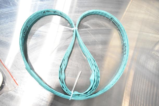 Teal rubber band coil with warning labels on a metallic surface. Part of Vevor HC-250 Commercial Bone Saw Machine's components.