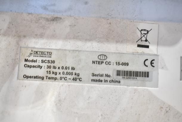 Detecto SCS30 produce scale label showing model, capacity (30 lb x 0.01 lb), and operating temperature range (0°C to 40°C).