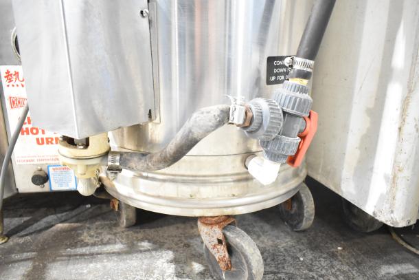 Oscar Fisher stainless steel tank, used, with visible hoses and valve connections. Signs of wear on wheels.